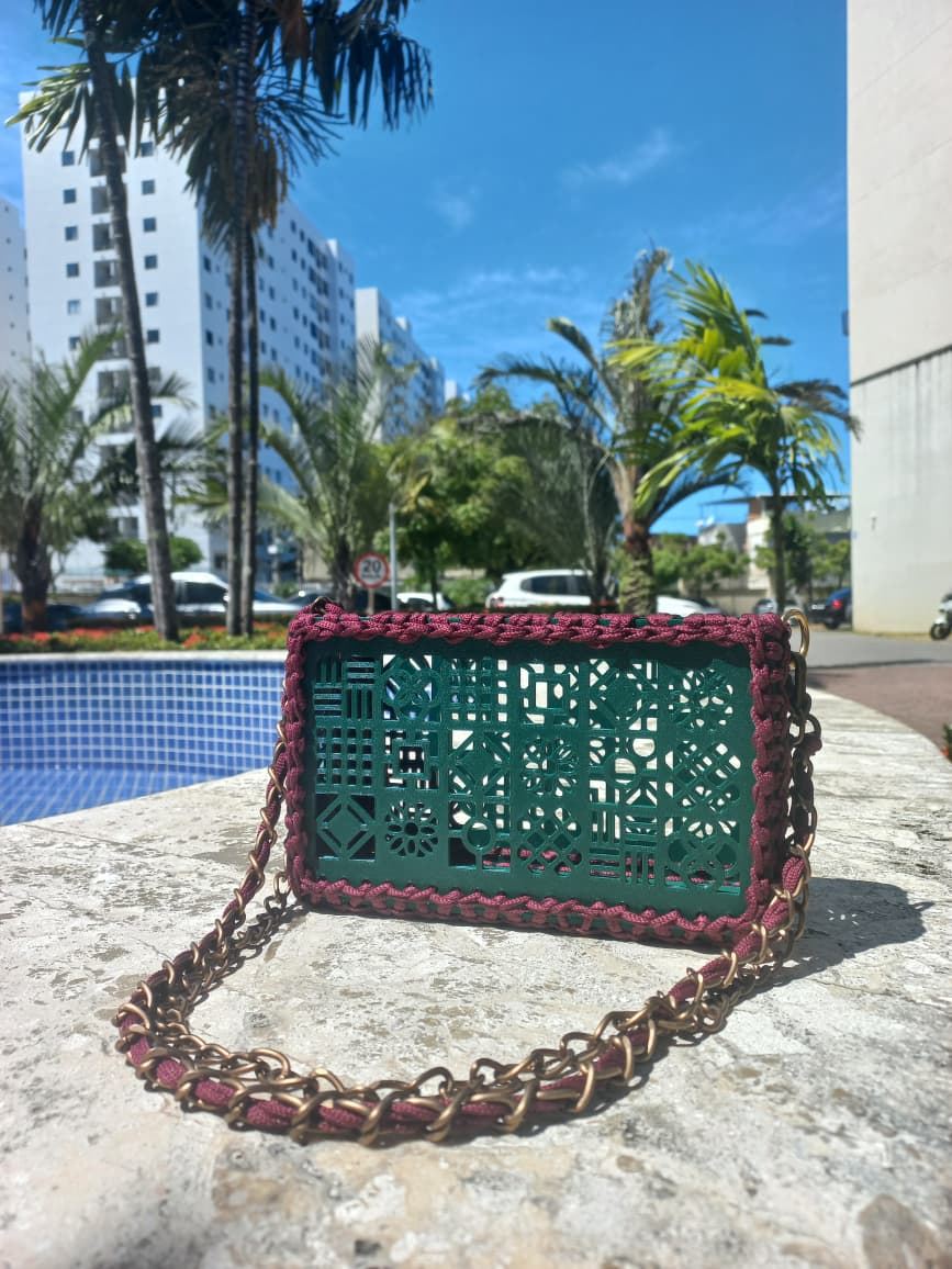 Bolsa com painel verde vazado em desenhos de cobogó, borda vinho e alça de corrente